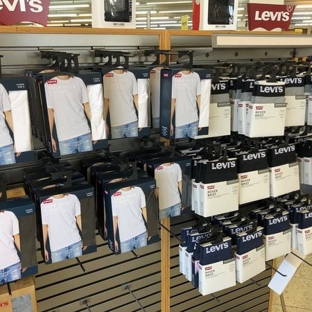 Verkaufswand mit Levis T-Shirts. Verpackte weiße Levis T-Shirts hängen ordentlich nebeneinander an Haken. Die Verpackungen zeigen ein Model mit dem jeweiligen Shirt.