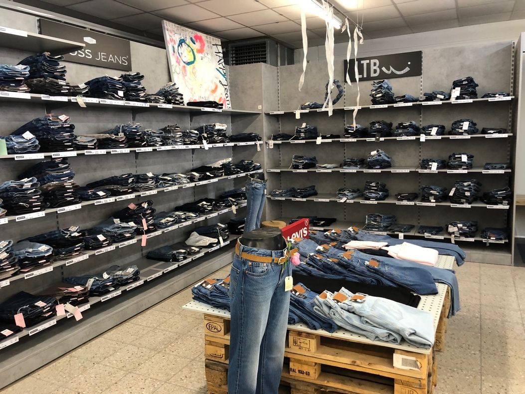 Jeansabteilung mit Markenbereich. Verkaufsfläche mit zahlreichen gefalteten Jeans der Marken Boss Jeans und LTB. In der Mitte steht ein Jeansmodell auf einer Palette, umgeben von weiteren gefalteten Hosen.