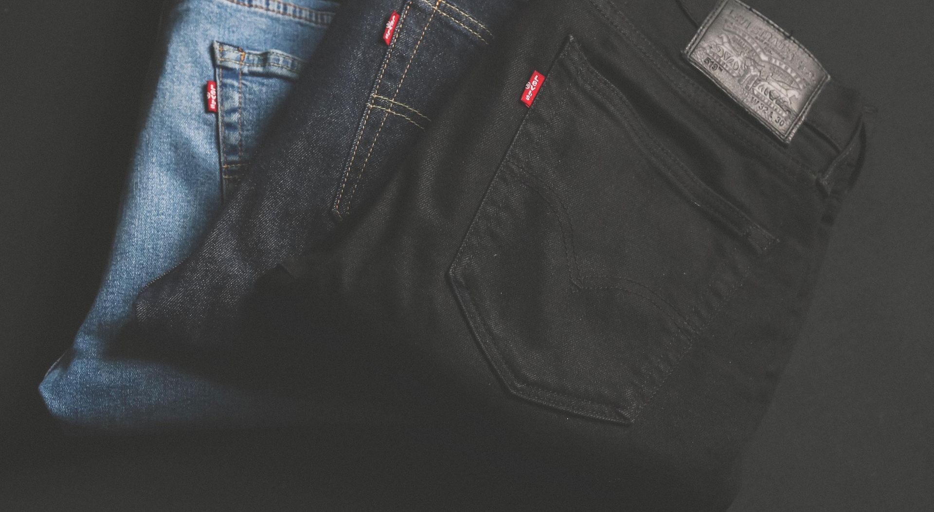 Drei gefaltete Levi's Jeans in unterschiedlichen Farben - hellblau, dunkelblau und schwarz - mit sichtbarem roten Markenlabel und Lederpatch